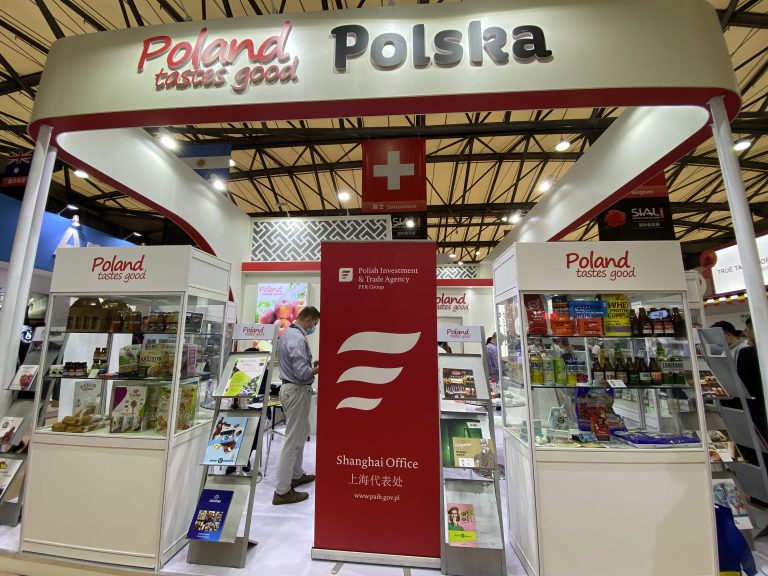 Zdjęcie przedstawia polskie stoisko narodowe na targach Sial China 2021. Na stoisku przeważają kolory biały i czerwony. Na fryzie stoiska dobrze widoczne logotypy Polska i Poland tastes good. Na stoisku przedstawiciele polskich firm promują swoje produkty. Stoisko cieszy się dużym zainteresowaniem zwiedzających.