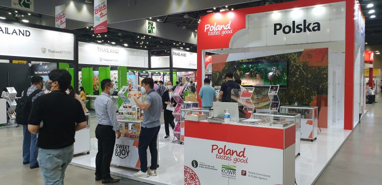 Zdjęcie przedstawia polskie stoisko narodowe na targach Seoul Food & Hotel 2021. Na stoisku przeważają kolory biały i czerwony. Na fryzie stoiska dobrze widoczne logotypy Polska i Poland tastes good.