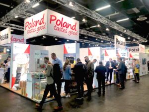 Zdjęcie przedstawia polskie stoisko narodowe. Na stoisku przeważają kolory biały i czerwony. Na fryzie stoiska dobrze widoczne logotypy Polska i Poland tastes good. Na stoisku przedstawiciele polskich firm promują swoje produkty. Stoisko cieszy się dużym zainteresowaniem zwiedzających.