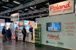 Zdjęcie przedstawia polskie stoisko narodowe. Na stoisku przeważają kolory biały i czerwony. Na fryzie stoiska dobrze widoczne logotypy Polska i Poland tastes good. Na stoisku przedstawiciele polskich firm promują swoje produkty. Stoisko cieszy się dużym zainteresowaniem zwiedzających.