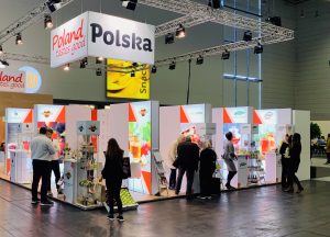 Zdjęcie przedstawia polskie stoisko narodowe. Na stoisku przeważają kolory biały i czerwony. Na fryzie stoiska dobrze widoczne logotypy Polska i Poland tastes good. Na stoisku przedstawiciele polskich firm promują swoje produkty. Stoisko cieszy się dużym zainteresowaniem zwiedzających.