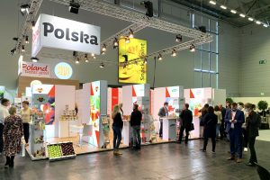 Zdjęcie przedstawia polskie stoisko narodowe. Na stoisku przeważają kolory biały i czerwony. Na fryzie stoiska dobrze widoczne logotypy Polska i Poland tastes good. Na stoisku przedstawiciele polskich firm promują swoje produkty. Stoisko cieszy się dużym zainteresowaniem zwiedzających.