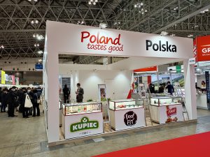 Zdjęcie przedstawia polskie stoisko narodowe. Na stoisku przeważają kolory biały i czerwony. Na fryzie stoiska dobrze widoczne logotypy Polska i Poland tastes good.